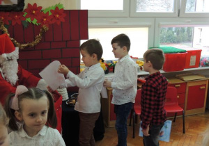 chłopcy stoją w kolejce do Mikołaja ze swoimi pracami i wkładają je do worka, który trzyma Mikołaj